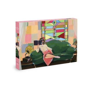 A puzzle box featuring an illustration of a woman reading on a green sofa, with a stained glass window and a gramophone in the background.