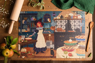 A completed jigsaw puzzle showing a woman baking in a kitchen is on a wooden table, surrounded by apples, a rolling pin, a spoon, and a green cloth.