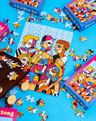 A completed 99-piece puzzle with an abstract, colorful illustration of four people, surrounded by loose puzzle pieces and puzzle boxes on a blue surface.
