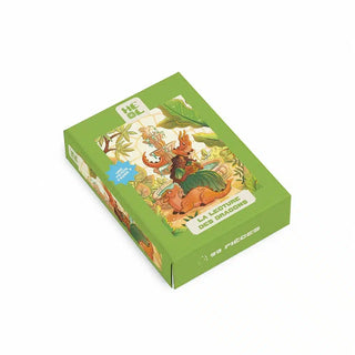 Green box for the La Lecture des Dragons | 99 Piece Jigsaw Puzzle, featuring an illustration of a woman reading to dragons by a fountain.