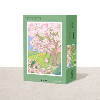 The Ber Good Spring Scenery 500 Piece Jigsaw Puzzle comes in a green rectangular box and features a blooming cherry blossom tree in a spring landscape, perfect for nature lovers seeking relaxing fun.