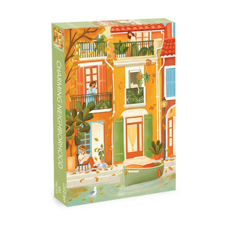 The Charming Neighborhood 500 Piece Jigsaw Puzzle by Olleo Puzzles features Yael Hofris vibrant village scene with apartments, balconies, lush plants, and a canal.