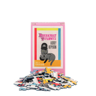 A box labeled “Breakfast At Tifurny’s” from Happily Jigsaw Puzzles, featuring a delightful cat illustration by Nia Gould, sits with its 99 mini jigsaw puzzle pieces scattered in front—a charming collectible perfect for film lovers and cat enthusiasts alike.