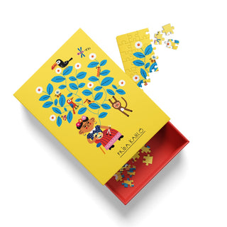The Ohh Deer “Frida Kahlo | 99 Piece Jigsaw Puzzle” features a vibrant yellow box adorned with an illustration of a woman, animals, and lush plants, capturing a floral masterpiece. With the lid open to reveal puzzle pieces inside and a partially assembled section on top, this set is perfect for art history puzzle enthusiasts.