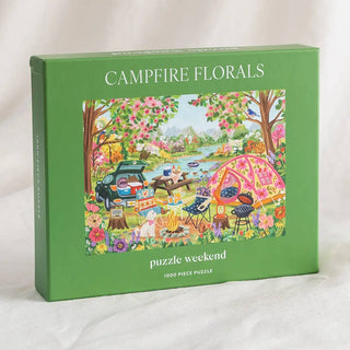 The green box labeled “Campfire Florals | 1,000 Piece Jigsaw Puzzle” by Puzzle Weekend features an illustrated picnic scene with a tent, car, food, and flowers; inside is a 1,000-piece camping-themed puzzle.