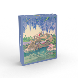 The Kibifufu Wisteria 1,008 Piece Jigsaw Puzzle features an arched wooden bridge over a pond with blooming wisteria and lush greenery. Completed puzzle measures 19.7" x 27.6".