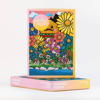 A 2,000-piece jigsaw puzzle from Sunshine Puzzles called “The Visitor,” featuring a colorful illustration of cartoon flowers, a small house, and a blue sky with the text “Sunshine Puzzles” in a pink circle, made from recycled waste paper.