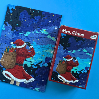 A partially assembled Mrs. Claus | 99 Piece Jigsaw Puzzle beside its box, both showing an illustration of Mrs. Claus in a red dress carrying a sack of gifts under a dark, starry sky.
