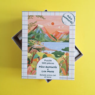 The "Balade Entre Ciel Et Terre" 500-piece jigsaw puzzle by Pièce Rapportée features vibrant landscape art with mountains, water, and buildings set against a yellow background.