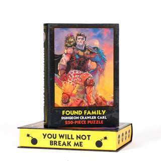 A boxed Found Family | 250 Piece Jigsaw Puzzle by Kingdom of Threads is stacked on top of a keepsake book box with the title You Will Not Break Me visible on the spine.