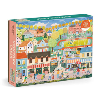 The Galison Hometown Cheer 1,000 Piece Jigsaw Puzzle features an illustrated small town scene with shops, houses, people, and trees on the box.