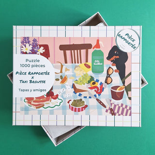 Tapas Y Amigos by Pièce Rapportée is a 1,000-piece jigsaw puzzle featuring an illustrated Spanish tapas table with food, drinks, dominoes, and a dog. Made in France, it comes partially open on a green background.