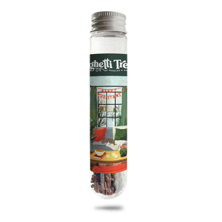 A clear test tube with a silver cap, featuring a decorative “Cozy Christmas” label from Spaghetti Tree, holds a 150-piece mini jigsaw puzzle—perfect for bringing portable puzzle fun wherever you go.