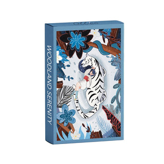 A blue rectangular box labeled “Woodland Serenity | 99 Piece Jigsaw Puzzle” by Olleo Puzzles features a white tiger holding a girl amid blue and brown foliage, capturing the charm of an enchanted forest.