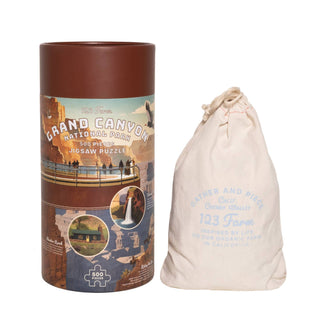 A cylindrical box labeled "Grand Canyon | 500 Piece Jigsaw Puzzle" from 123 Farm sits beside a drawstring cloth bag marked with the brand name.