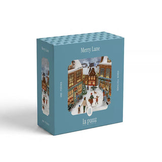 A blue box of the la pauz Merry Lane 280-piece jigsaw puzzle, showcasing an illustrated winter village scene with people strolling by snow-covered buildings—a charming holiday puzzle perfect for celebrating the season.