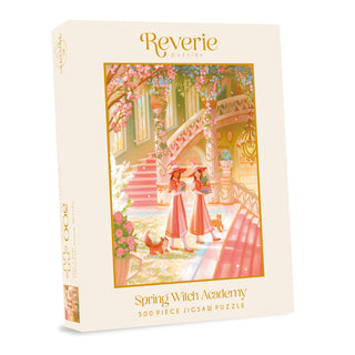 Spring Witch Academy | 500 Piece Jigsaw Puzzle by Reverie Puzzles comes in a box featuring an enchanting pastel illustration of two witches and a cat at a spring-themed academy.