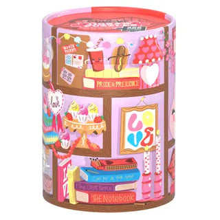 The “Objects of My Affection | 200 Piece Jigsaw Puzzle” by Chronicle Books comes in a colorful cylindrical container adorned with whimsical illustrations of books, cupcakes, and romantic-themed decorations set against a pink background. This delightful puzzle contains 200 pieces and is FSC certified.