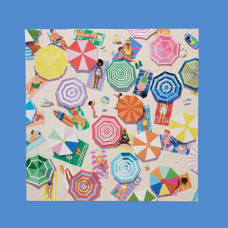 Enjoy a vibrant aerial view of beachgoers relaxing under colorful umbrellas in WerkShoppe’s Beach Day | 1,000 Piece Jigsaw Puzzle, made from recycled board and featuring scattered towels and accessories on sandy shores.