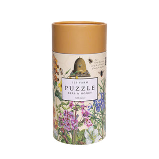 The 123 Farm Bees & Honey | 500 Piece Jigsaw Puzzle comes in a cylindrical box featuring charming nature illustrations of flowers, bees, and a beehive inspired by an organic farm.