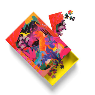 The Prehistoric Carnivores | 99 Piece Jigsaw Puzzle by Ohh Deer features a vibrant, dinosaur-themed design with colorful dinosaurs and lush plants set against a cheerful yellow interior; loose pieces surround the partially completed puzzle, making it an ideal choice for adult jigsaw enthusiasts and T-Rex fans alike.