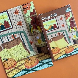 A partially assembled Cozy Fall | 99 Piece Jigsaw Puzzle by Puzzledly featuring a cozy bedroom scene with pumpkins and autumn leaves, shown next to its box.