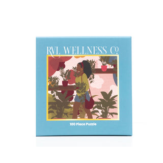 The Ayanna | 100 Piece Jigsaw Puzzle by RVL Wellness Co. comes in a blue box and features an illustration of a woman holding plants, surrounded by greenery and potted plants.