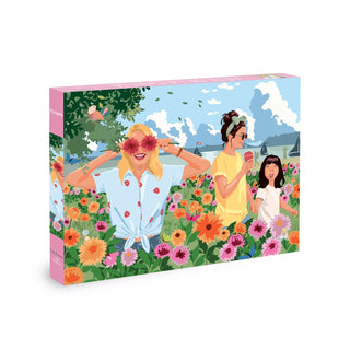 Enjoy a vibrant scene from the Dahlia Festival | 500 Piece Jigsaw Puzzle by Olleo Puzzles, featuring an illustration of three people in a lively dahlia field inspired by the famous Dahlia Festival of Morges near Lake Geneva: one person playfully holds flowers over her eyes, another sips from a cup, while a child stands nearby—set against a background of blue sky and fluffy clouds.