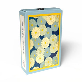 The Flower Umbrellas | 99 Piece Jigsaw Puzzle by Penny Puzzle comes in a light blue rectangular box decorated with yellow-centered blue and white Meiji-style flowers, evoking the look of a vintage Japanese puzzle.