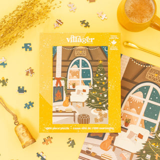 The Fireside Christmas 1,000-piece jigsaw puzzle by Villager Puzzles features a cozy Canadian holiday living room scene displayed on a yellow surface with loose pieces, a brass bell, tea cup, and dried flowers.