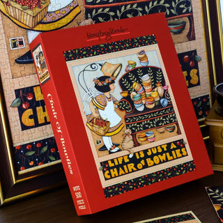 Here’s the rewritten sentence incorporating your product data: The Chair of Bowlies | 500 Piece Jigsaw Puzzle by WEVE features Mary Engelbreit's charming artwork of a woman holding fruit beside a chair with bowls, set amid art supplies and a completed puzzle showing the same delightful scene. Crafted from premium blue board for durability, this puzzle offers both quality and engaging imagery.