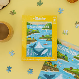 The Newfoundland Sites | 500 Piece Jigsaw Puzzle by Villager Puzzles sits on a yellow surface with loose pieces, part of the puzzle completed, coffee, and cookies—making it a unique Canadian souvenir or cozy coastal decor for your home.