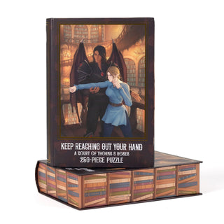 Kingdom of Threads Keep Reaching Out Your Hand 250 Piece Jigsaw Puzzle depicting a winged man and a woman in a library, designed with book-spine edges.