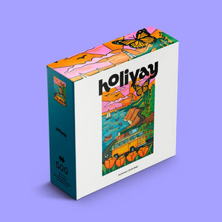 Sur La Route | 500 Piece Jigsaw Puzzle by Holiyay Puzzles features colorful, hand-drawn art of a butterfly, a van on a coastal road, pumpkins, and a sunset by a Chicago illustrator. Brand name is displayed on the box front.