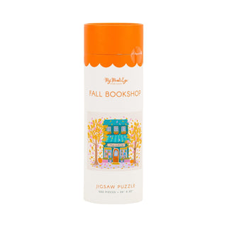 Cylindrical container with an orange lid, labeled “Fall Bookshop | 500 Piece Jigsaw Puzzle” by My Mind’s Eye, featuring a charming illustration of a small bookshop surrounded by autumn trees. This cozy 500-piece puzzle is perfect for relaxing afternoons.