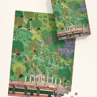 The Trinity Bellwoods | 1,000 Piece Jigsaw Puzzle by Mango Puzzles, featuring a vibrant park scene with trees, people, and a streetcar, sits beside its box—with both capturing Toronto's lively charm.