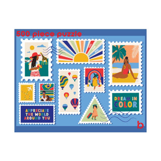 The Be Rooted World Traveler | 500 Piece Jigsaw Puzzle comes in a travel-friendly box and features vibrant, stamp-style illustrations of people, hot air balloons, a rainbow, and uplifting messages like “DREAM IN COLOR” and “APPRECIATE THE WORLD AROUND YOU.” Perfect for anyone inspired by adventure and the beauty of discovery.