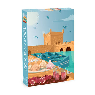 Experience the charm of Morocco's coastal town with Olleo Puzzles' "Windy Essaouira" 500-piece jigsaw puzzle, featuring a detailed illustration of boats, a historic stone building, seagulls, and a seaside table adorned with pastries, pomegranates, and drinks.
