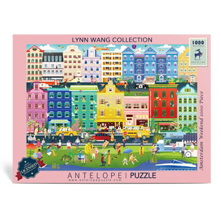 Antelope Puzzle’s "Amsterdam Weekend | 1,000 Piece Jigsaw Puzzle" features colorful illustrations of a vibrant city scene with multicolored buildings, people, cars, and cyclists from Lynn Weilin’s Cactus series.