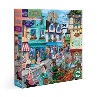 The eeBoo "Village by the Sea" 1,000 piece jigsaw puzzle features a colorful illustrated seaside village street with shops, pedestrians, and cyclists.