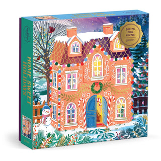 The Home Sweet Holidays 500 Piece Jigsaw Puzzle from Chronicle Books features a vibrant illustrated gingerbread house adorned with festive decorations, snow, trees, and a cheerful snowman.