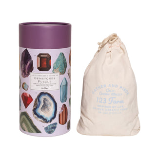 The 123 Farm Gemstones | 500 Piece Jigsaw Puzzle comes in a cylindrical box with gemstone and nature designs, along with a cream drawstring bag labeled 123 Farm—ideal for puzzle storage.