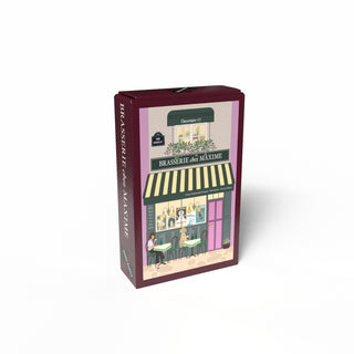The Penny Puzzle "Brasserie Chez Maxime" 99-piece jigsaw features a rectangular box with an illustrated Parisian café storefront and people seated outside, capturing the city’s charm in a delightful mini puzzle.