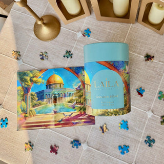 A Laila Luxury Puzzles Golden Dome 500-piece jigsaw puzzle sits on a table beside a Palestine puzzle guide with a dome illustration, surrounded by loose pieces from the Ola El-Metwally design.