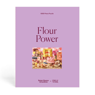 A purple box holds the Flour Power | 1,000 Piece Jigsaw Puzzle by Piecework Puzzles, featuring cakes and pastries inspired by vintage cookbooks, with logos for Better Homes & Gardens and Piecework at the bottom.