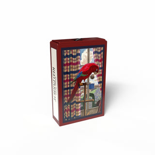The Penny Puzzle "Red Parrot" is a 99 piece jigsaw puzzle in a rectangular box featuring a vintage-style illustration of a red parrot perched indoors by a window with striped curtains and trees visible outside.