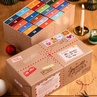 Two Trevell Advent Calendar No. 4 boxes from Trevell, each containing 24 mini 99-piece jigsaw puzzles in numbered compartments, are displayed on a wooden table with candles and ornaments.