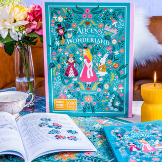 A delightful Bookworm Puzzles Alice’s Adventures in Wonderland | 500 Piece Jigsaw Puzzle Book Set is beautifully displayed on a floral table with an open book, candle, cup of tea, and vase of flowers—a perfect Lewis Carroll-inspired puzzle and book combo for fans of whimsical adventures.