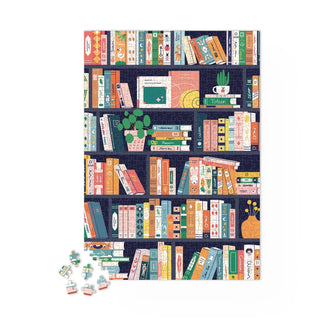 The Maison Joliette "Book Lovers" 1,000-piece jigsaw puzzle for adults showcases illustrated bookshelves with colorful books, plants, and decor—plus a few loose pieces nearby.