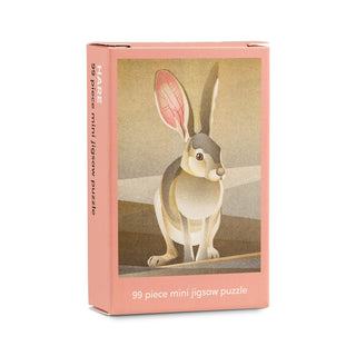 A pink box labeled “Hare | 99 Piece Mini Jigsaw Puzzle” by Happily Jigsaw Puzzles, featuring a charming hare illustration standing on a grassy patch and crafted from FSC paper.